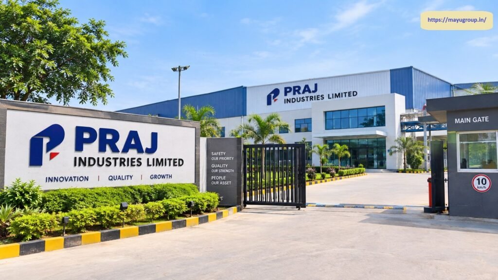 Exterior entrance view of the Praj Industries Limited facility featuring a large branded perimeter wall, security gate, main entrance, and corporate facility building under a clear blue sky.
